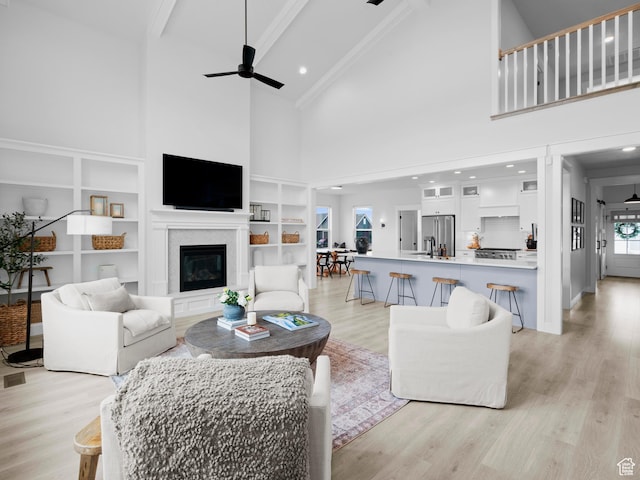 living room featuring high vaulted ceiling, ceiling fan, light wood finished floors, a glass covered fireplace, and built in features