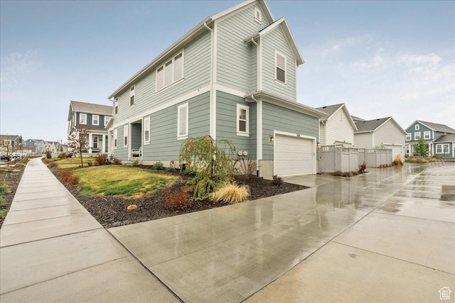 view of property exterior featuring fence, driveway, a residential view, and a garage
