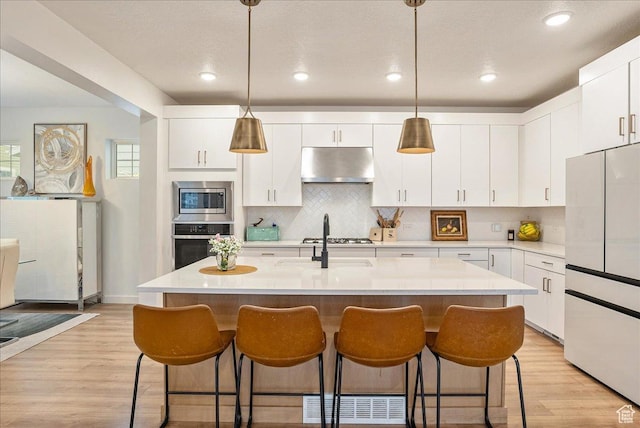 kitchen with under cabinet range hood, appliances with stainless steel finishes, a kitchen bar, and light countertops