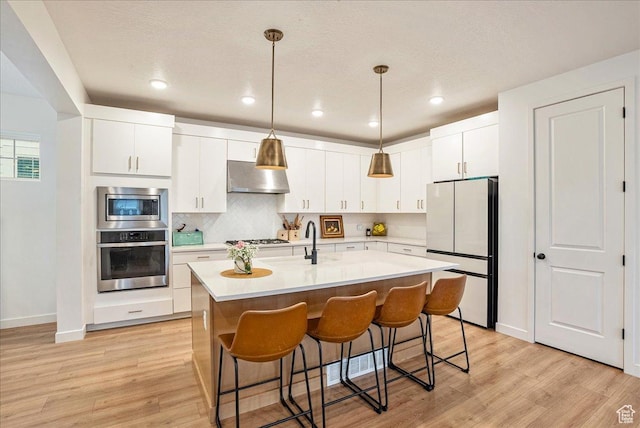 kitchen featuring stainless steel appliances, light countertops, light wood-style floors, wall chimney exhaust hood, and baseboards