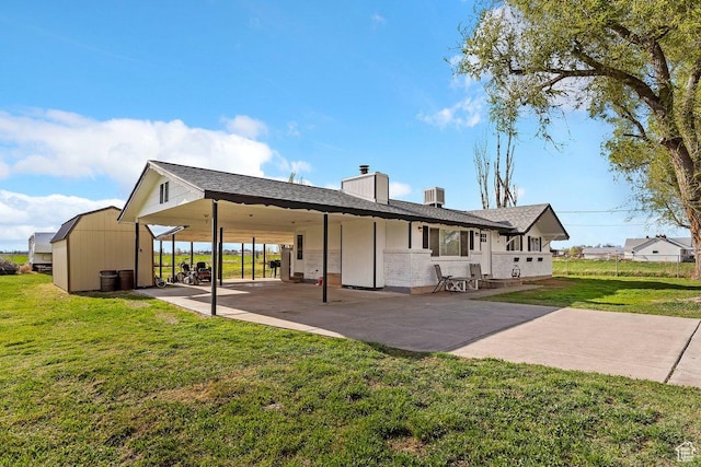 back of property with an attached carport, a chimney, concrete driveway, a patio area, and a lawn
