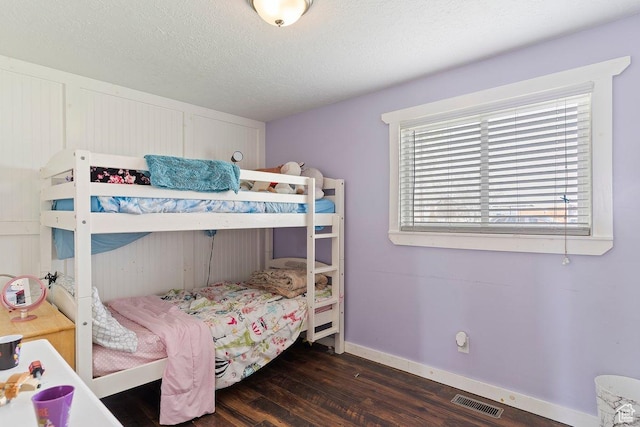 bedroom with a textured ceiling, wood finished floors, visible vents, and baseboards