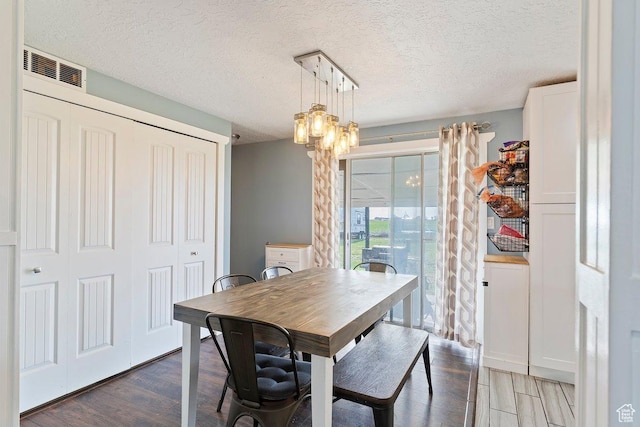 dining space with a chandelier, a textured ceiling, wood finished floors, and visible vents