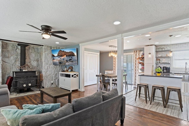 living room with recessed lighting, wood finished floors, a wood stove, a textured ceiling, and ceiling fan with notable chandelier