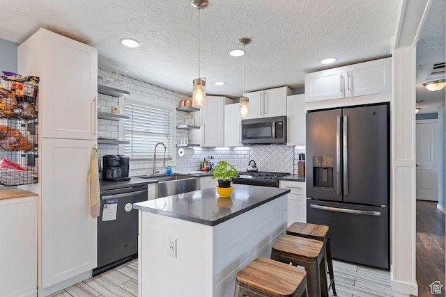 kitchen featuring white cabinets, stainless steel appliances, open shelves, dark countertops, and a sink