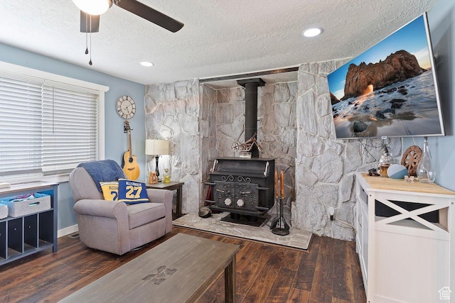 living area featuring wood finished floors, a wood stove, a textured ceiling, and ceiling fan