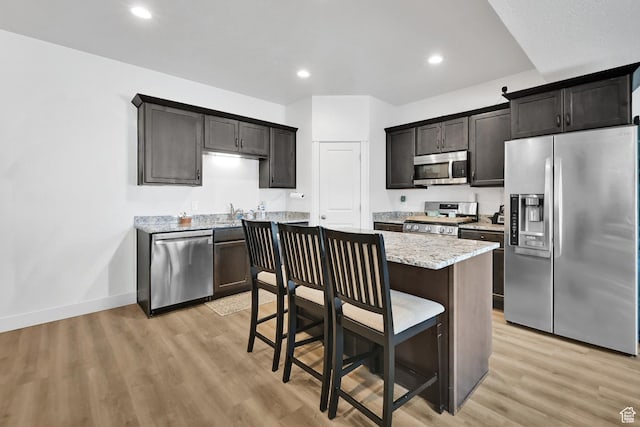 kitchen featuring light wood finished floors, a breakfast bar, baseboards, light stone countertops, and appliances with stainless steel finishes