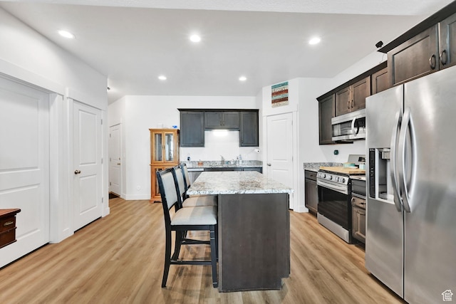 kitchen featuring a breakfast bar, light stone counters, light wood finished floors, a kitchen island, and appliances with stainless steel finishes