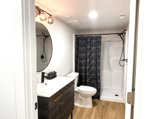 full bath featuring wood finished floors, visible vents, vanity, walk in shower, and a textured ceiling