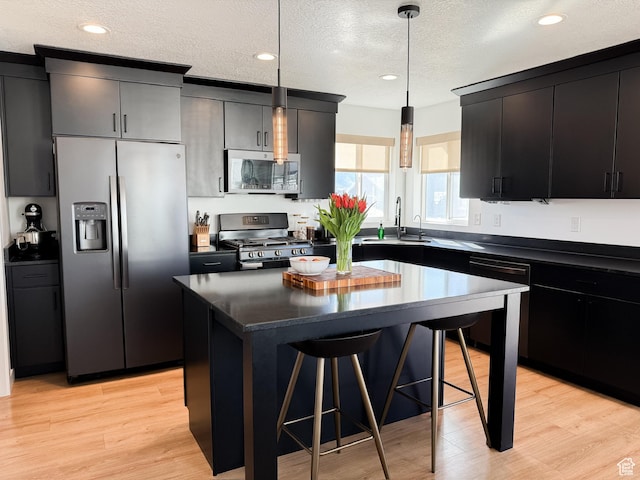 kitchen with a breakfast bar, dark countertops, a sink, a textured ceiling, and appliances with stainless steel finishes