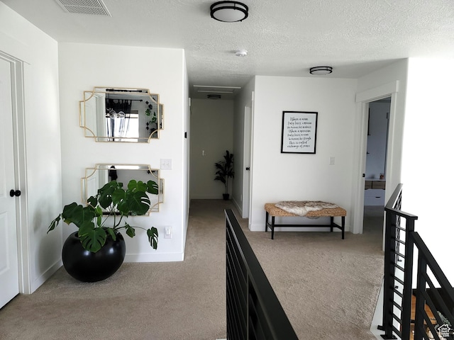hall featuring a textured ceiling, carpet, visible vents, and baseboards