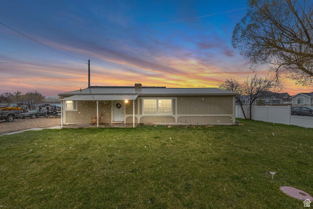 back of property at dusk featuring metal roof, a yard, a chimney, and fence