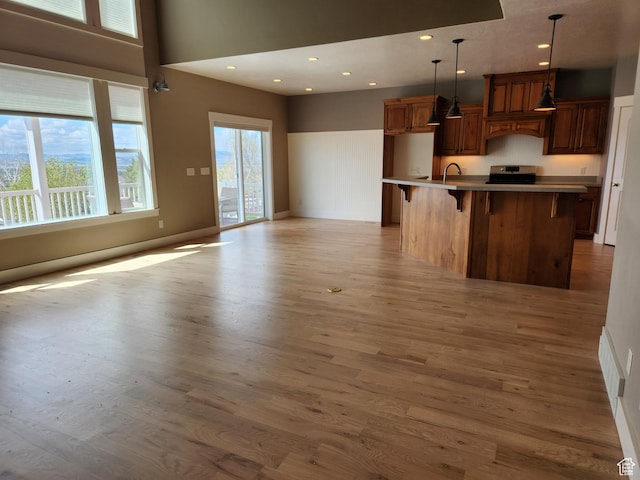 kitchen with stainless steel electric range oven, light wood-type flooring, a kitchen breakfast bar, decorative light fixtures, and a sink
