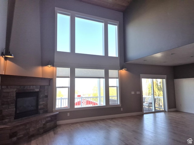 unfurnished living room featuring wood finished floors, baseboards, a stone fireplace, and a high ceiling
