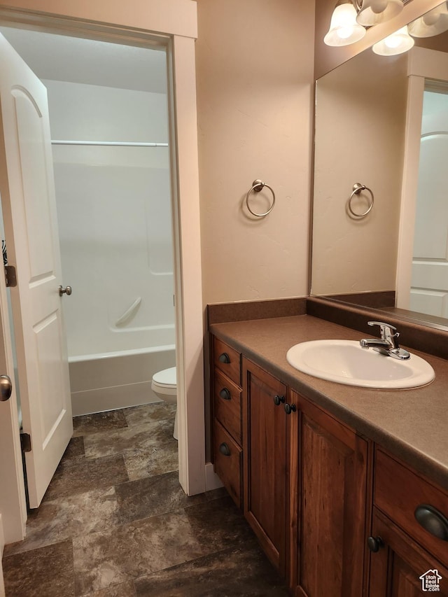 bathroom with toilet, vanity, stone finish floors, and tub / shower combination