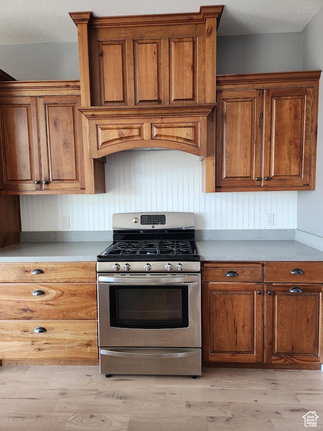 kitchen featuring stainless steel gas range oven, brown cabinetry, and light wood finished floors