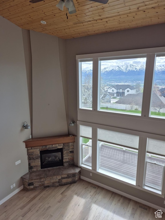 unfurnished living room featuring a ceiling fan, a stone fireplace, wood finished floors, baseboards, and wooden ceiling