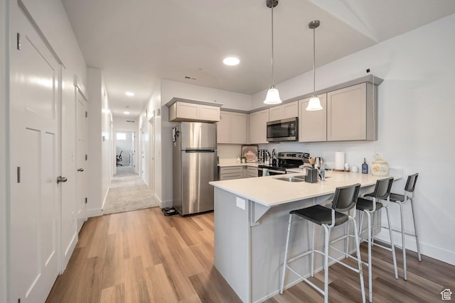 13537 S Commodus Dr W Unit 304, Riverton, UT 84096 - kitchen with stainless steel appliances, a peninsula, light wood-style flooring, a kitchen bar, and light countertops