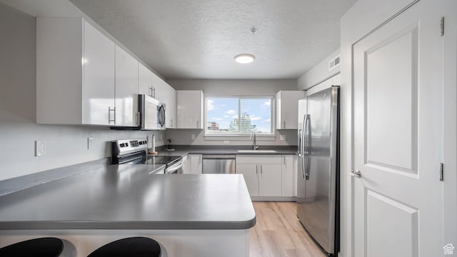 kitchen with a textured ceiling, a sink, light wood-style floors, stainless steel appliances, and a peninsula