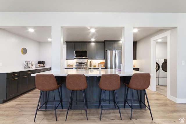6982 W Majestic View Ln S, Herriman, UT 84096 - kitchen with stainless steel appliances, light countertops, independent washer and dryer, tasteful backsplash, and light wood-style flooring