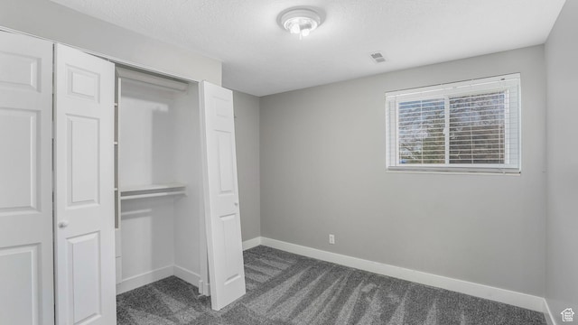 unfurnished bedroom with dark colored carpet, visible vents, a closet, baseboards, and a textured ceiling