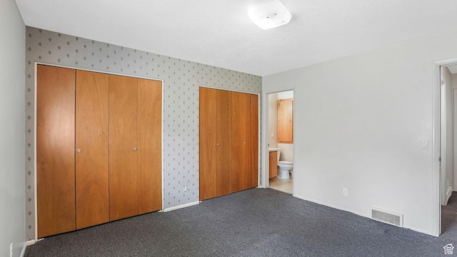 unfurnished bedroom with baseboards, visible vents, wallpapered walls, multiple closets, and ensuite bath