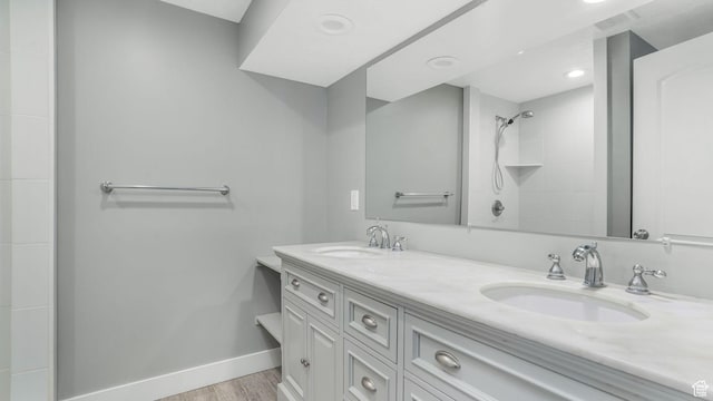 full bathroom featuring double vanity, wood finished floors, tiled shower, and a sink