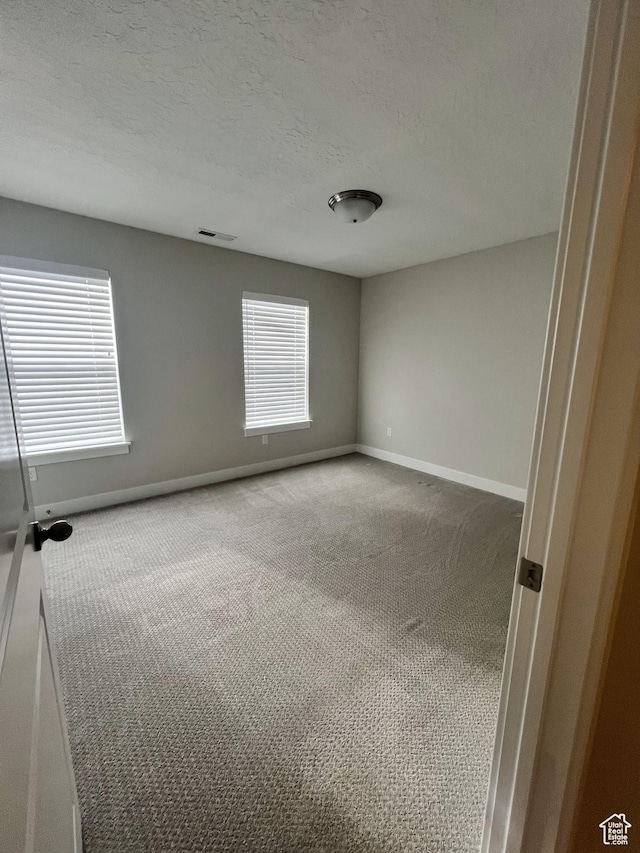 spare room with a textured ceiling, visible vents, carpet floors, and baseboards