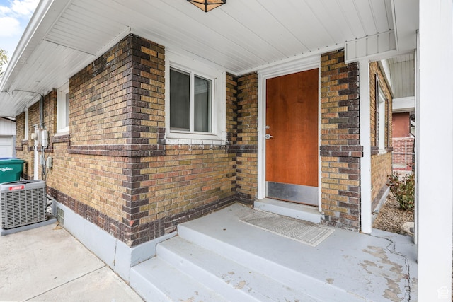 property entrance featuring central AC unit, brick siding, and a porch