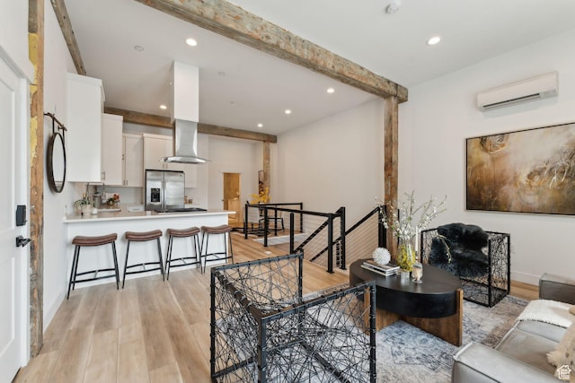 living area with a wall mounted AC, light wood-style flooring, beamed ceiling, recessed lighting, and baseboards