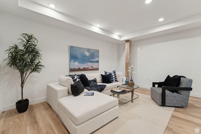 living room with light wood-type flooring, recessed lighting, baseboards, and a tray ceiling