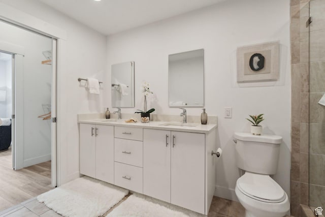 bathroom with toilet, double vanity, baseboards, and a tile shower