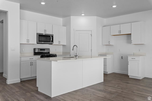 kitchen with white cabinets, stainless steel appliances, a kitchen island with sink, and dark wood-style floors