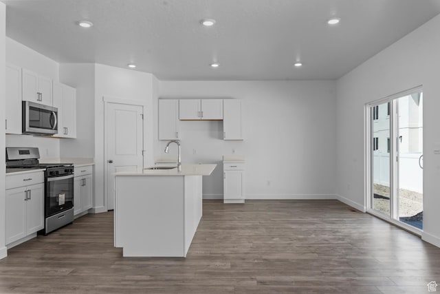 kitchen with dark wood finished floors, appliances with stainless steel finishes, a center island with sink, and white cabinetry