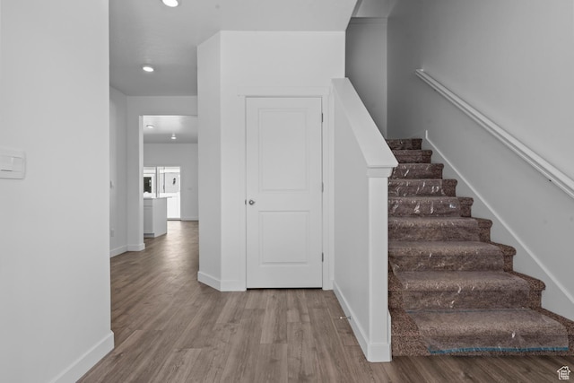 stairway with baseboards, wood finished floors, and recessed lighting