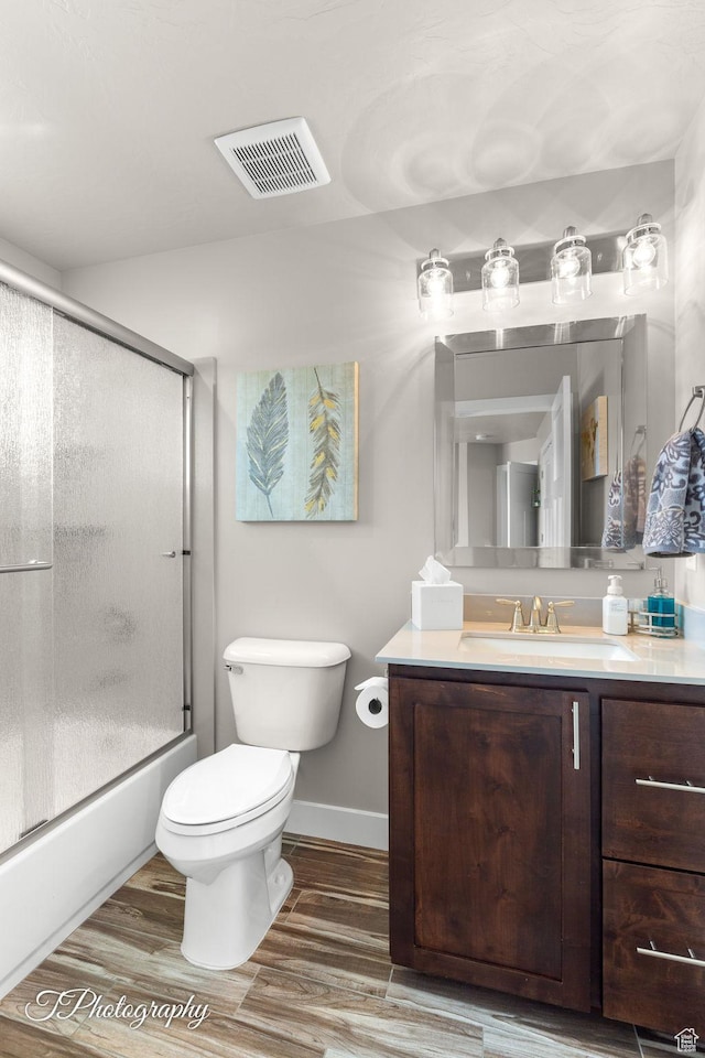 bathroom with wood finished floors, vanity, bath / shower combo with glass door, toilet, and visible vents