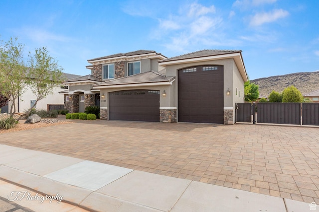 prairie-style house featuring a gate, stucco siding, decorative driveway, stone siding, and a garage