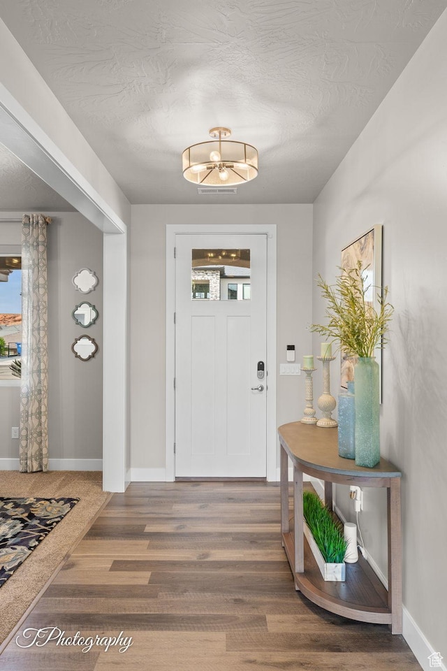 entryway with a chandelier, wood finished floors, a textured ceiling, and baseboards
