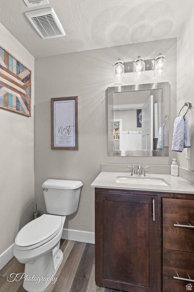 bathroom featuring toilet, baseboards, visible vents, wood finished floors, and vanity