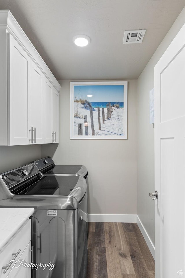 laundry room with washing machine and clothes dryer, cabinet space, dark wood finished floors, baseboards, and visible vents