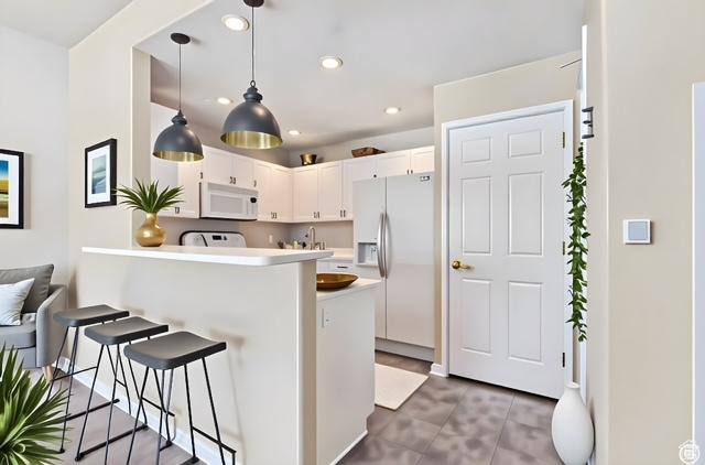 974 W Big River Ct Unit 2, South Salt Lake, UT 84119 - kitchen with a breakfast bar area, pendant lighting, a peninsula, white appliances, and white cabinetry