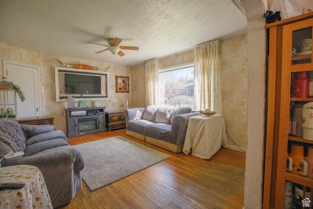 living area with ceiling fan, wood-type flooring, and a textured ceiling