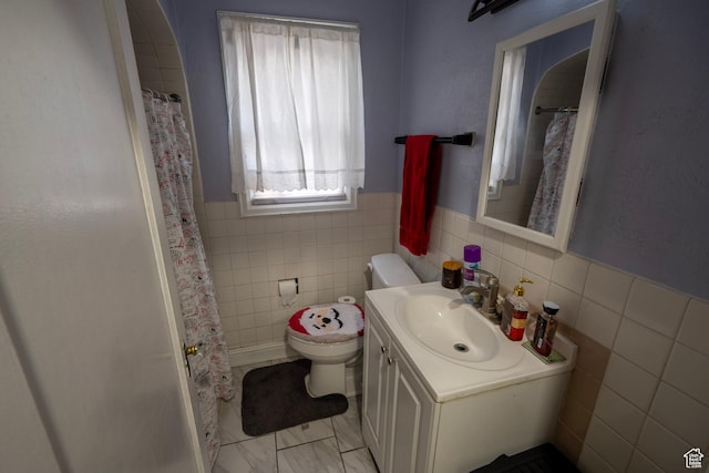 bathroom with toilet, tile walls, wainscoting, a shower with shower curtain, and vanity