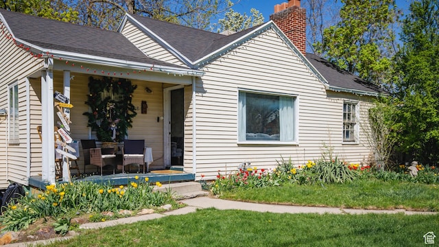 bungalow with a chimney, a front lawn, roof with shingles, and covered porch