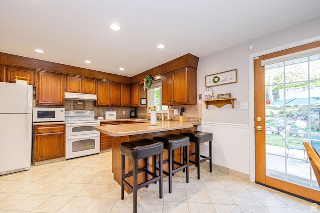 kitchen with a peninsula, white appliances, light countertops, under cabinet range hood, and tasteful backsplash