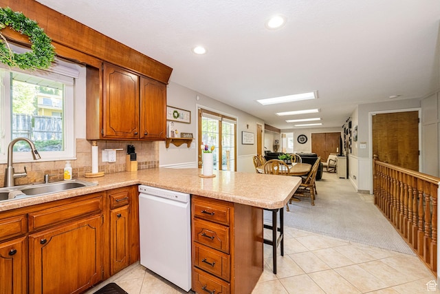 kitchen featuring a peninsula, light tile patterned flooring, light countertops, a sink, and dishwasher