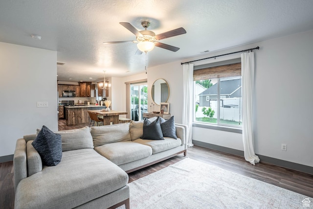 living room featuring wood finished floors, visible vents, baseboards, a textured ceiling, and ceiling fan with notable chandelier