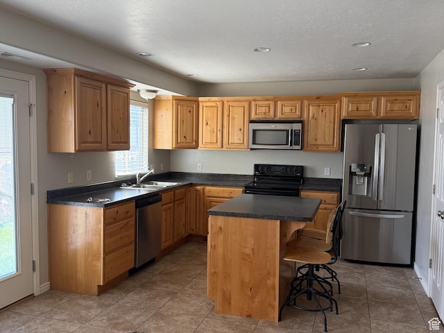 kitchen with dark countertops, a sink, a breakfast bar area, appliances with stainless steel finishes, and a kitchen island