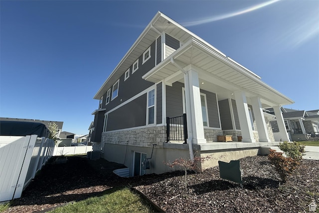 6129 W Coulee Ln, West Jordan, UT 84081 - view of side of property with central AC unit, stone siding, covered porch, and fence