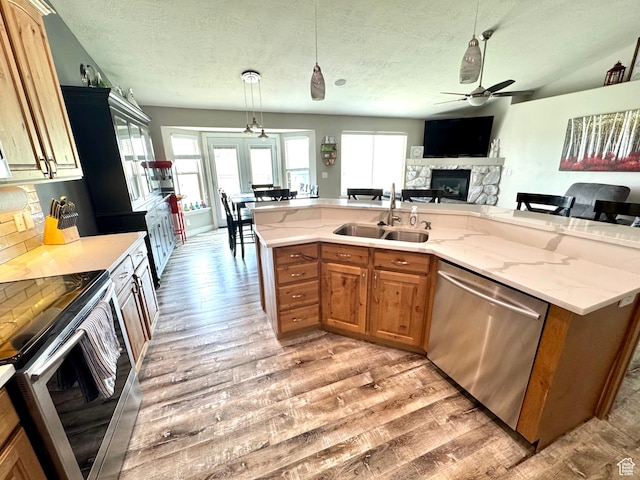 8675 N Franklin Dr E, Eagle Mountain, UT 84005 - kitchen with a ceiling fan, a sink, light wood-style flooring, a fireplace, and appliances with stainless steel finishes